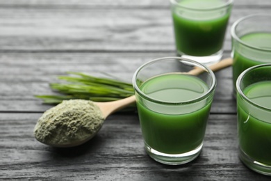 Photo of Glasses of wheat grass juice and spoon with powder on wooden table. Space for text