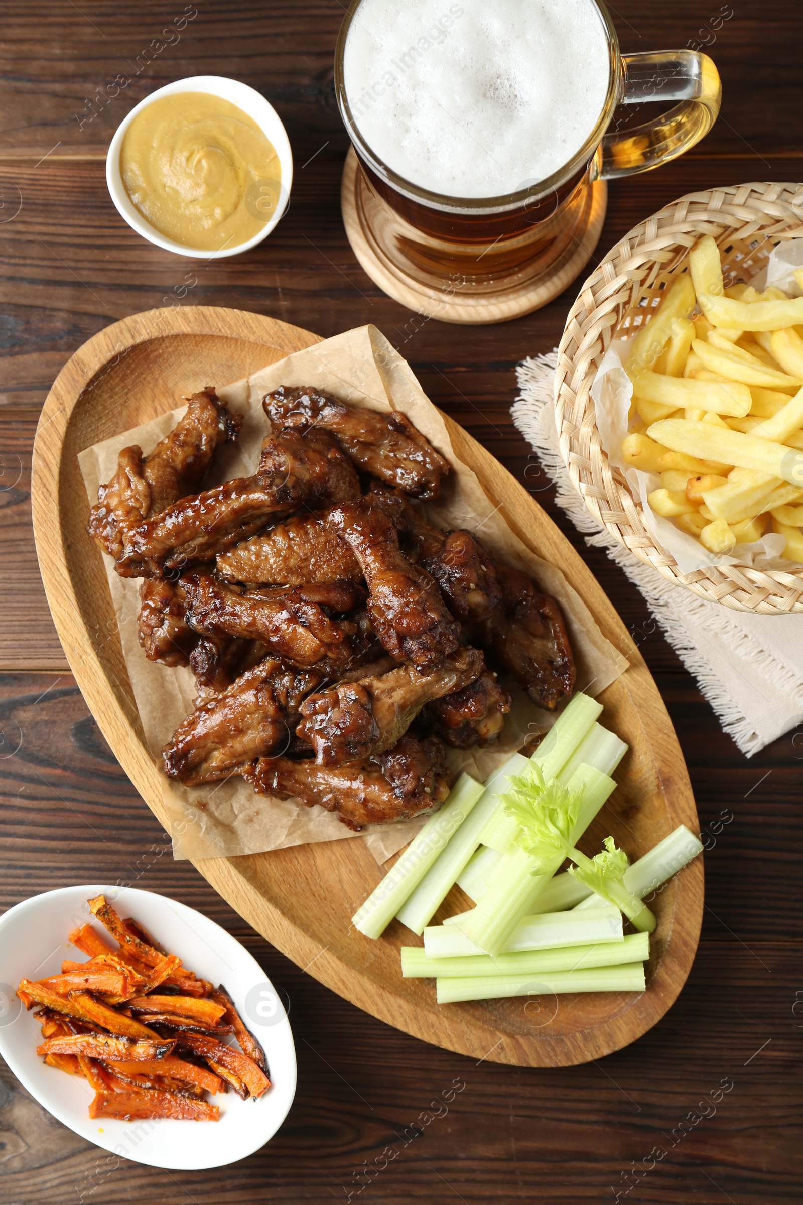 Photo of Delicious chicken wings served with beer on wooden table, flat lay