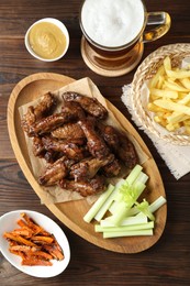 Photo of Delicious chicken wings served with beer on wooden table, flat lay