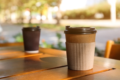 Photo of Cardboard coffee cup on wooden table outdoors. Space for text