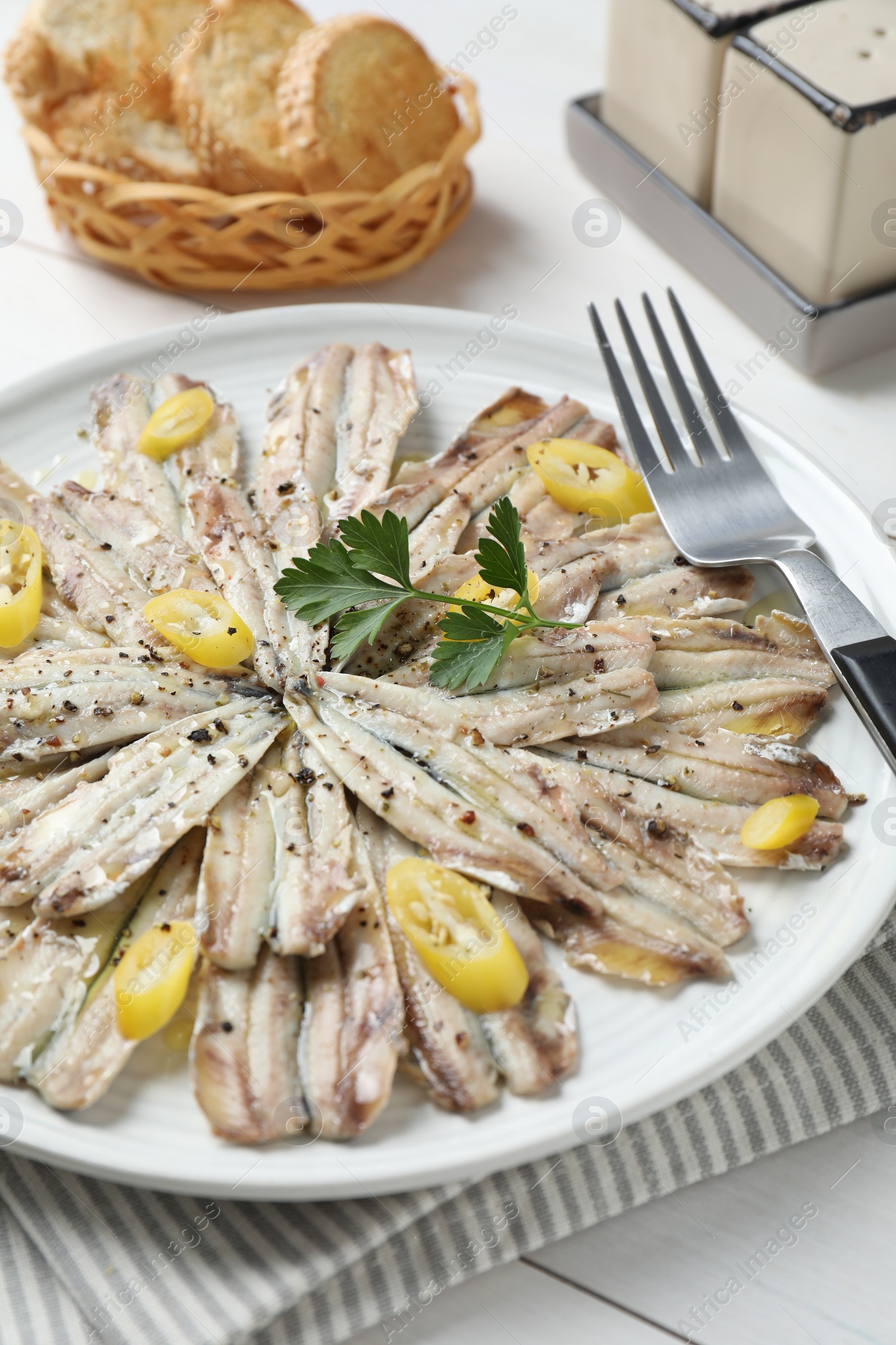 Photo of Tasty pickled anchovies with spices and fork on white wooden table, closeup