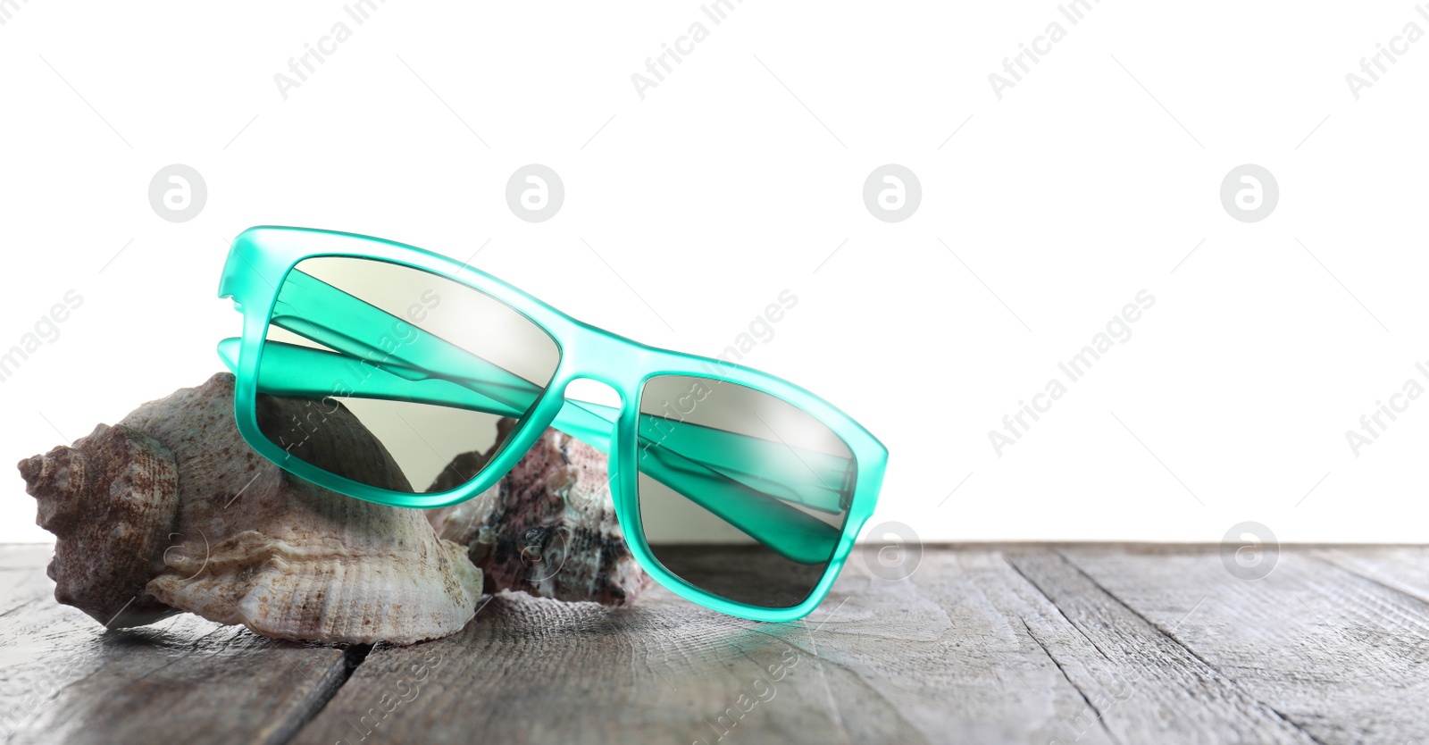 Photo of Stylish sunglasses and shells on wooden table against white background. Space for text