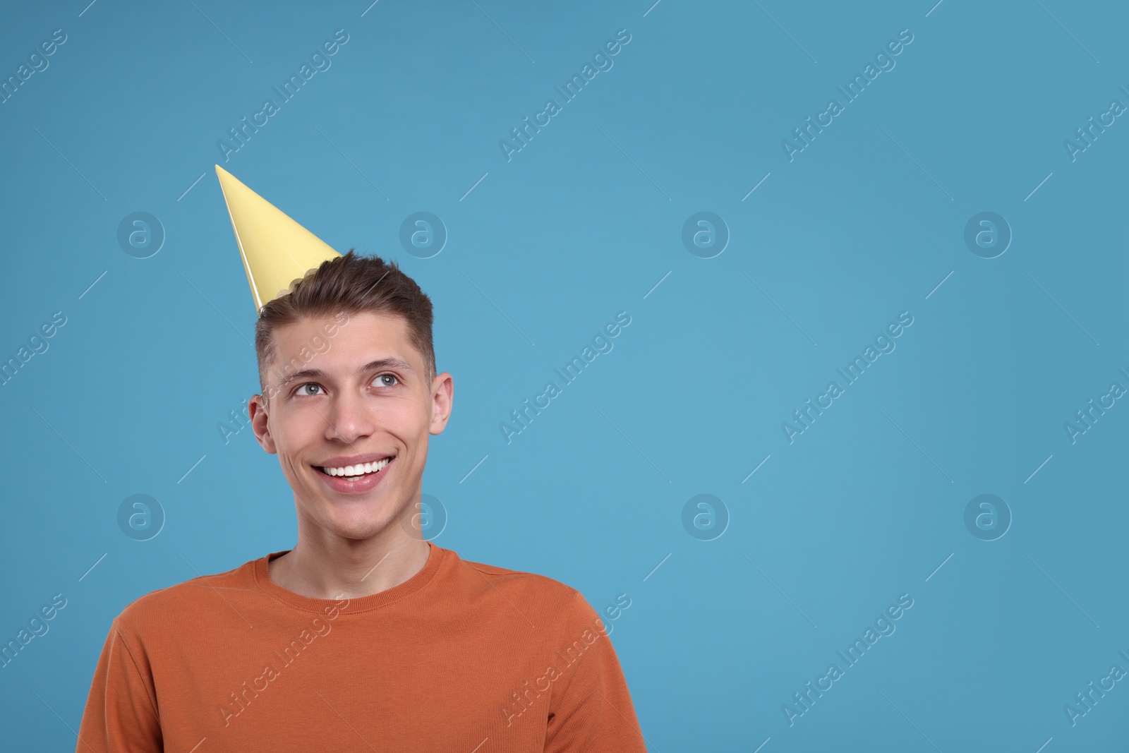 Photo of Happy man in party hat on light blue background. Space for text