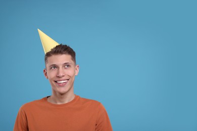Photo of Happy man in party hat on light blue background. Space for text