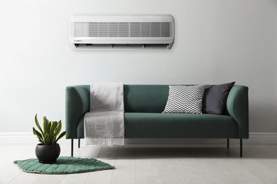 Image of Modern air conditioner on light wall in room with stylish sofa