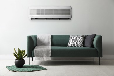 Modern air conditioner on light wall in room with stylish sofa