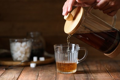 Photo of Woman pouring delicious tea into glass cup at wooden table, closeup. Space for text