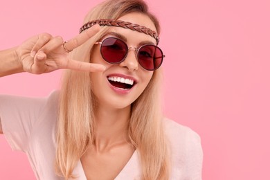 Photo of Portraitsmiling hippie woman showing peace sign on pink background. Space for text