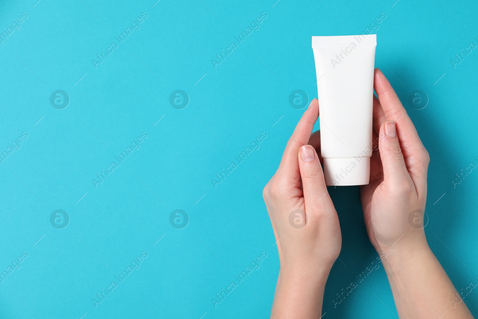 Photo of Woman with tube of hand cream on light blue background, top view. Space for text