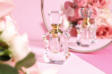 Photo of Bottle of perfume near mirror on pink background