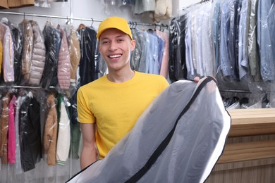 Happy courier holding garment cover with clothes in dry-cleaning