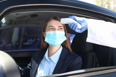 Photo of Doctor measuring woman's temperature with non contact infrared thermometer in car