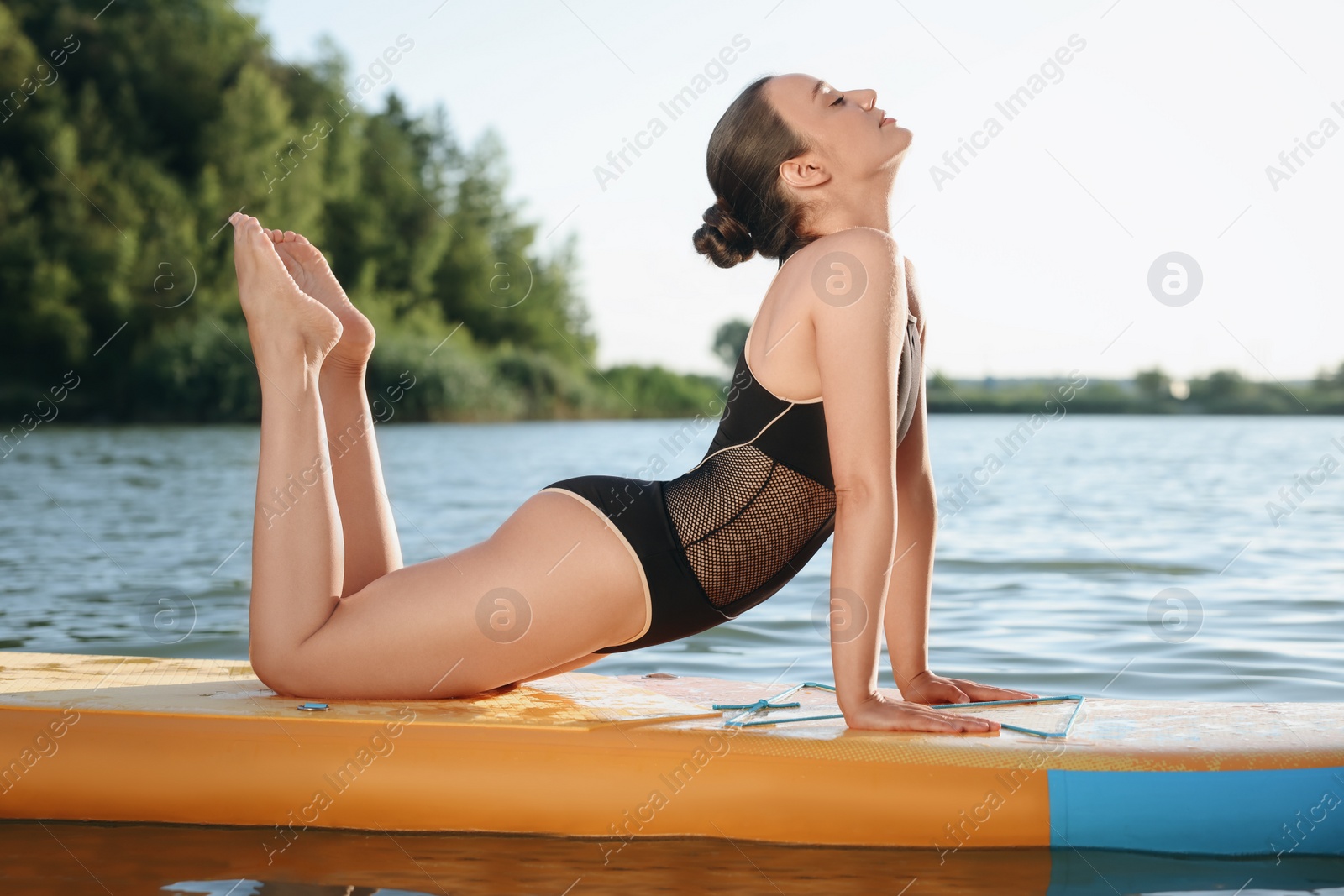 Photo of Young woman practicing yoga on color SUP board on river