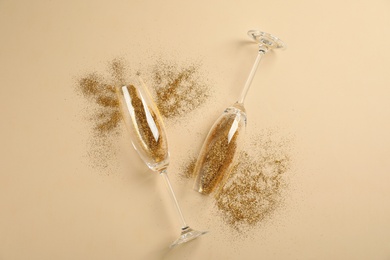 Photo of Champagne glasses with gold glitter on beige background, flat lay. Hilarious celebration