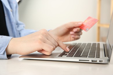 Photo of Online payment. Woman with credit card using laptop at white table indoors, closeup