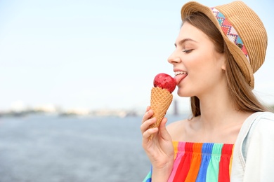 Young happy woman eating ice cream on riverside. Space for text