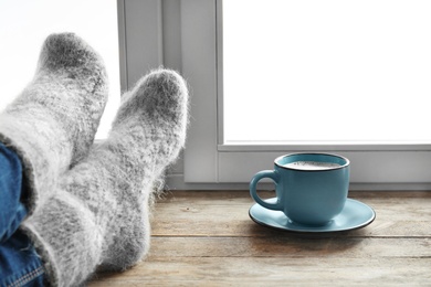Photo of Woman in warm socks and cup of hot winter drink on windowsill. Cozy season