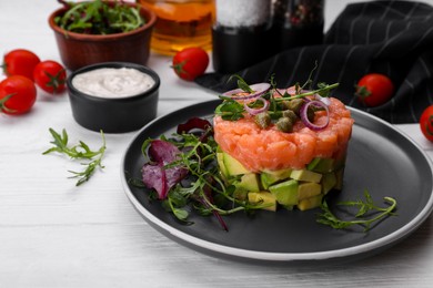 Photo of Tasty salmon tartare with avocado and greens on white wooden table. Space for text