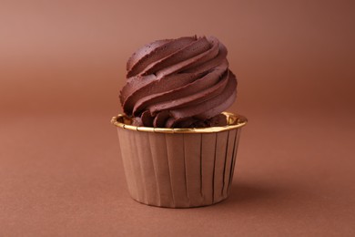 Delicious chocolate cupcake on brown background, closeup