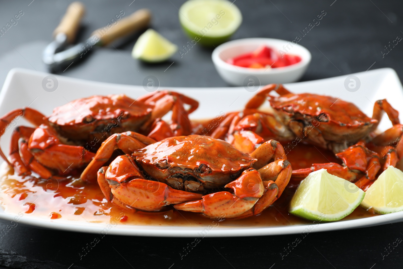 Photo of Delicious boiled crabs with sauce and lime on black table, closeup