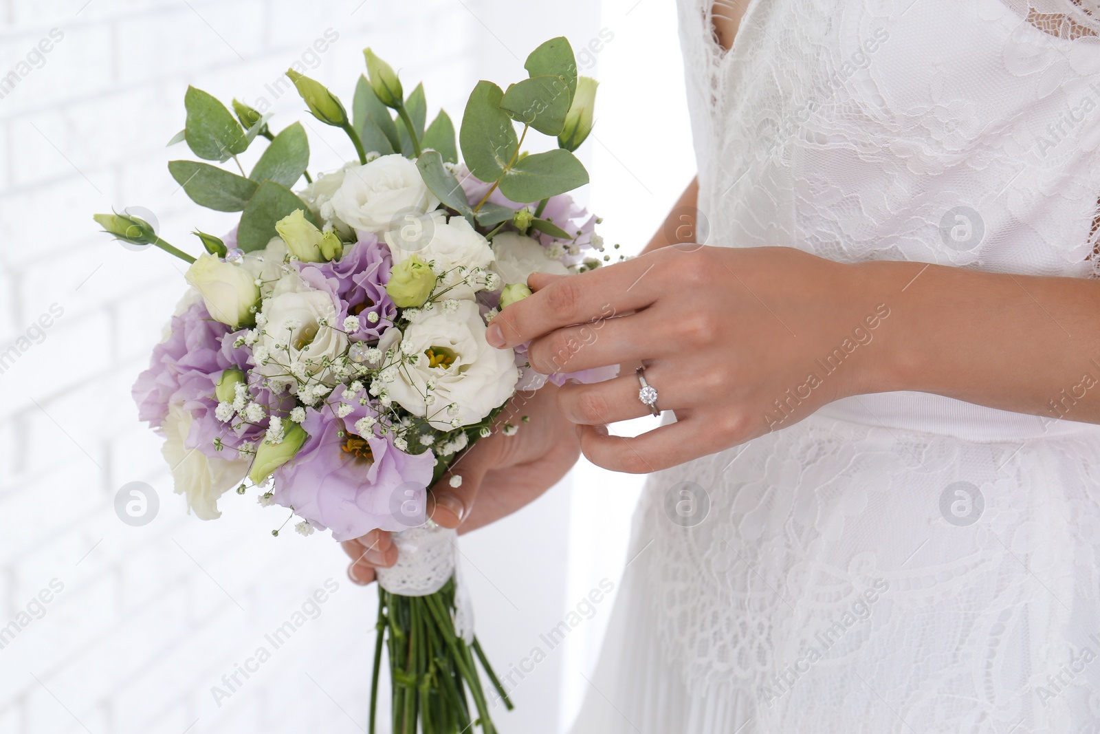 Photo of Bride holding beautiful bouquet with Eustoma flowers indoors, closeup