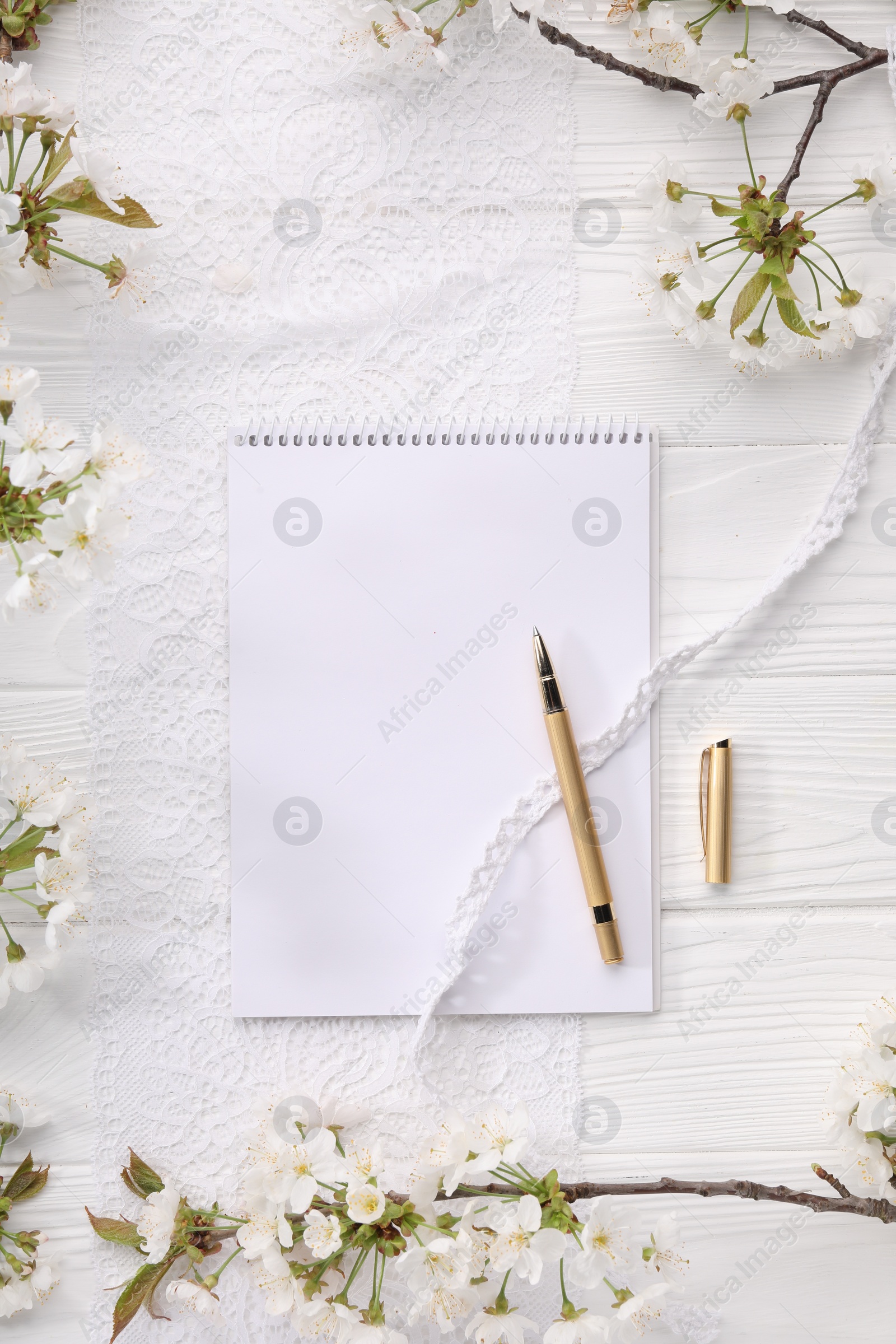 Photo of Guest list. Notebook, pen, spring tree branches with beautiful blossoms and lace ribbons on white wooden background, flat lay