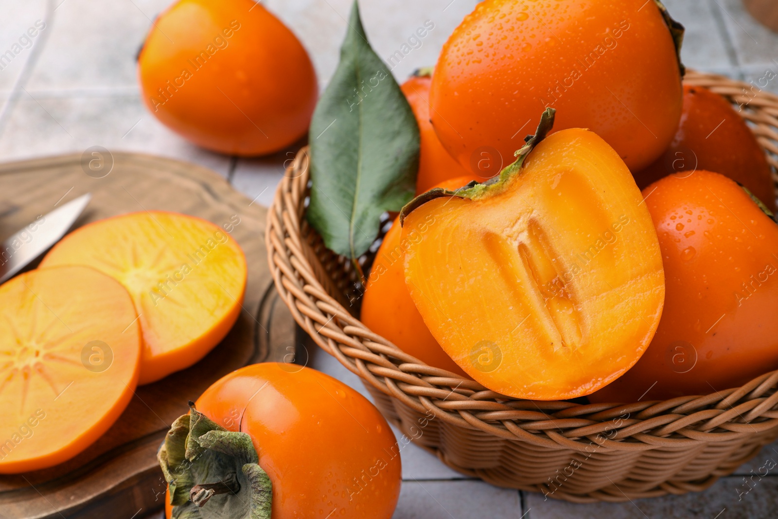 Photo of Delicious ripe juicy persimmons in wicker basket on tiled surface, closeup