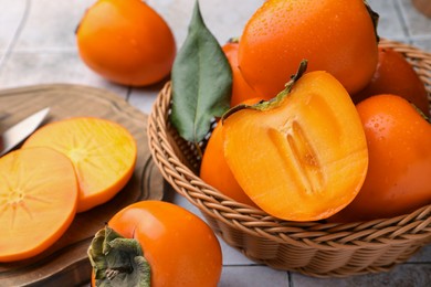 Photo of Delicious ripe juicy persimmons in wicker basket on tiled surface, closeup