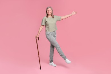 Senior woman with walking cane posing on pink background