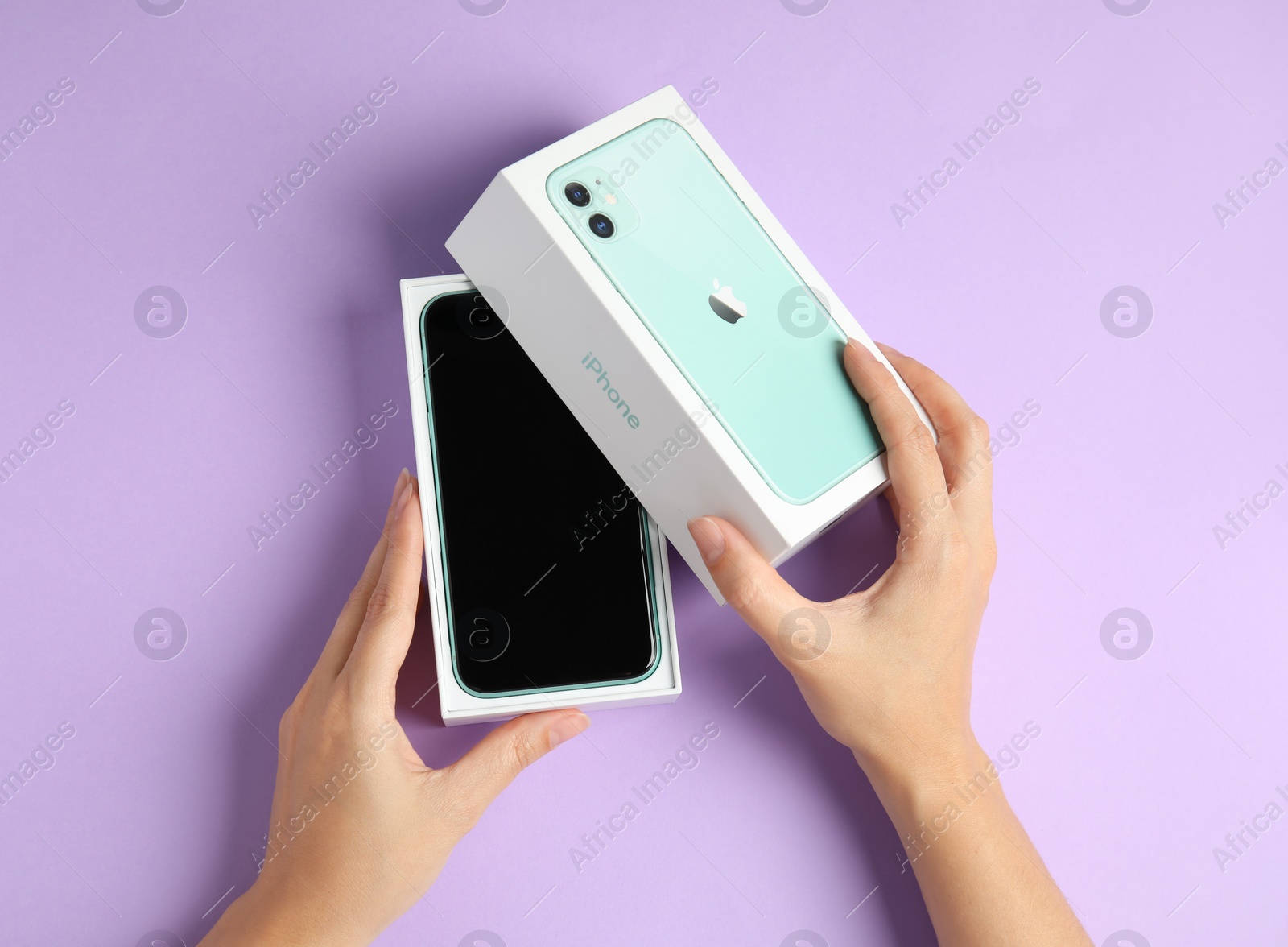 Photo of MYKOLAIV, UKRAINE - JULY 10, 2020: Woman opening box with Iphone 11 on violet background, top view