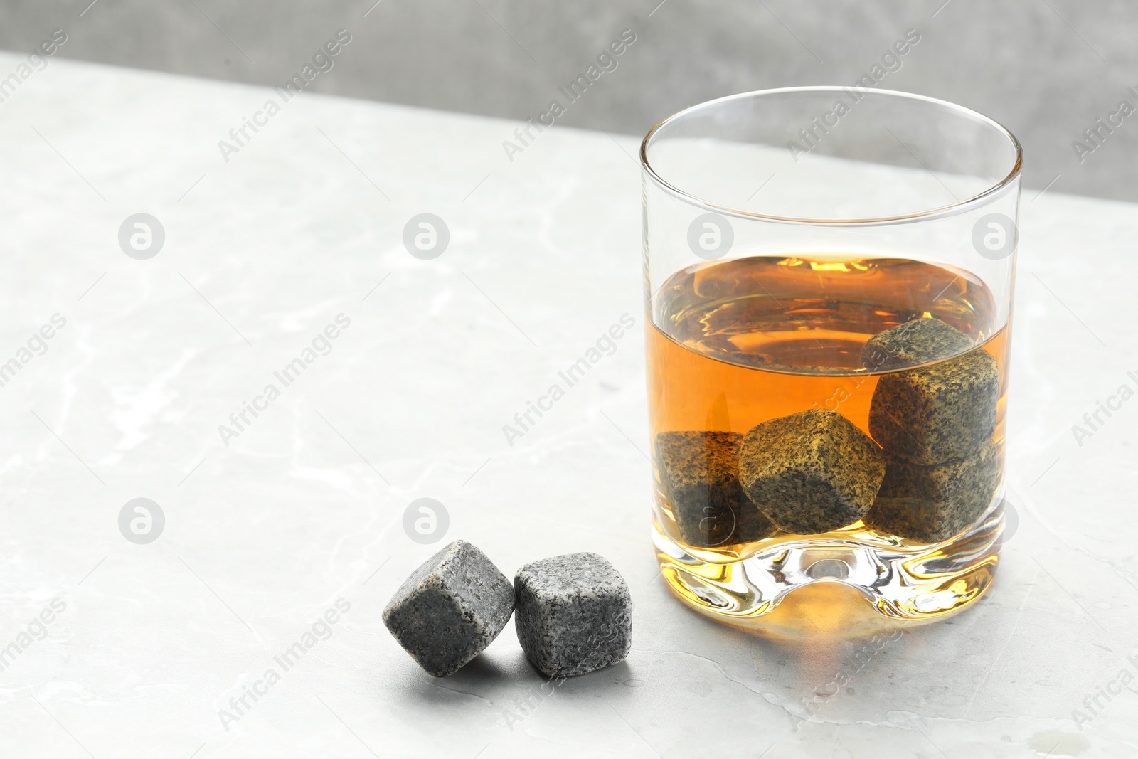 Photo of Whiskey stones and drink in glass on light marble table, closeup. Space for text