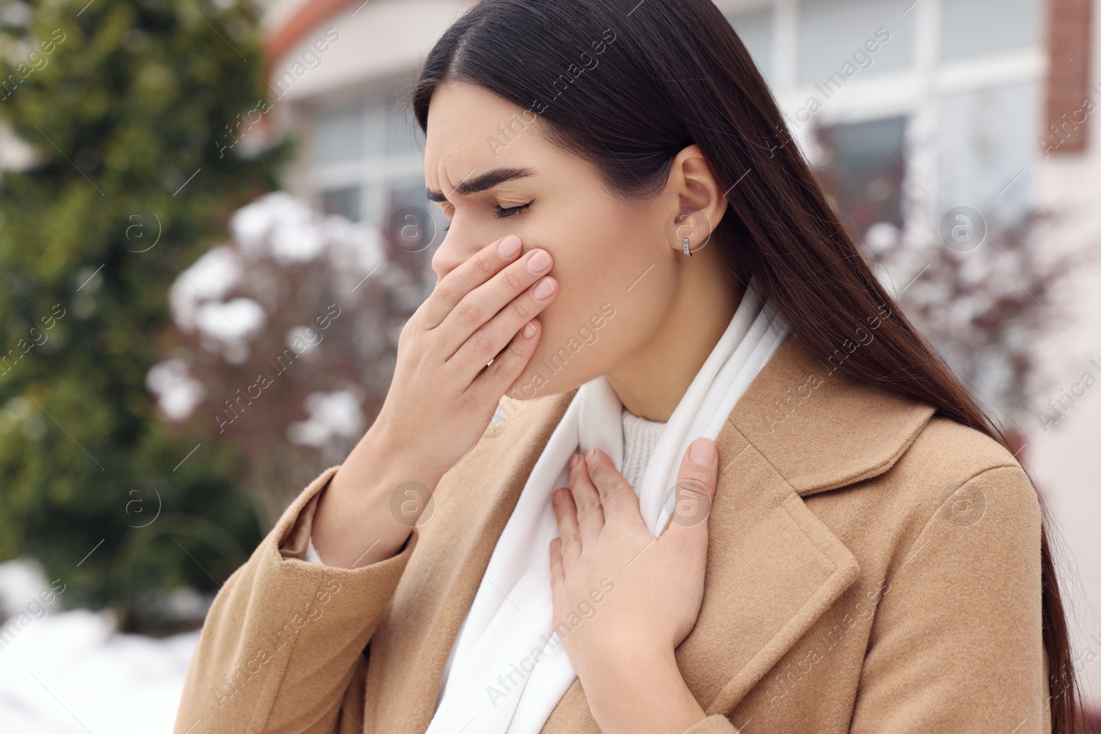 Photo of Woman in coat coughing outdoors. Cold symptoms