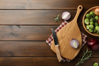 Cutting board with different vegetables, rosemary and knife on wooden table, flat lay. Space for text