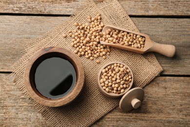 Soy sauce in bowl and soybeans on wooden table, flat lay