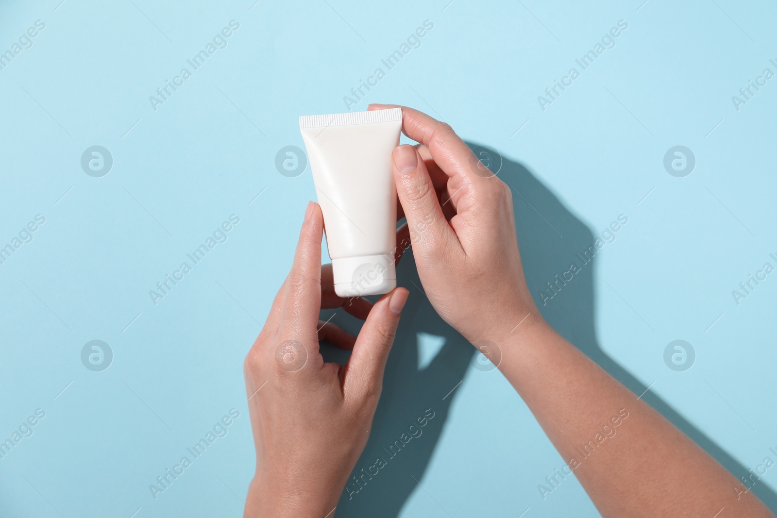 Photo of Woman with tube of hand cream on light blue background, top view