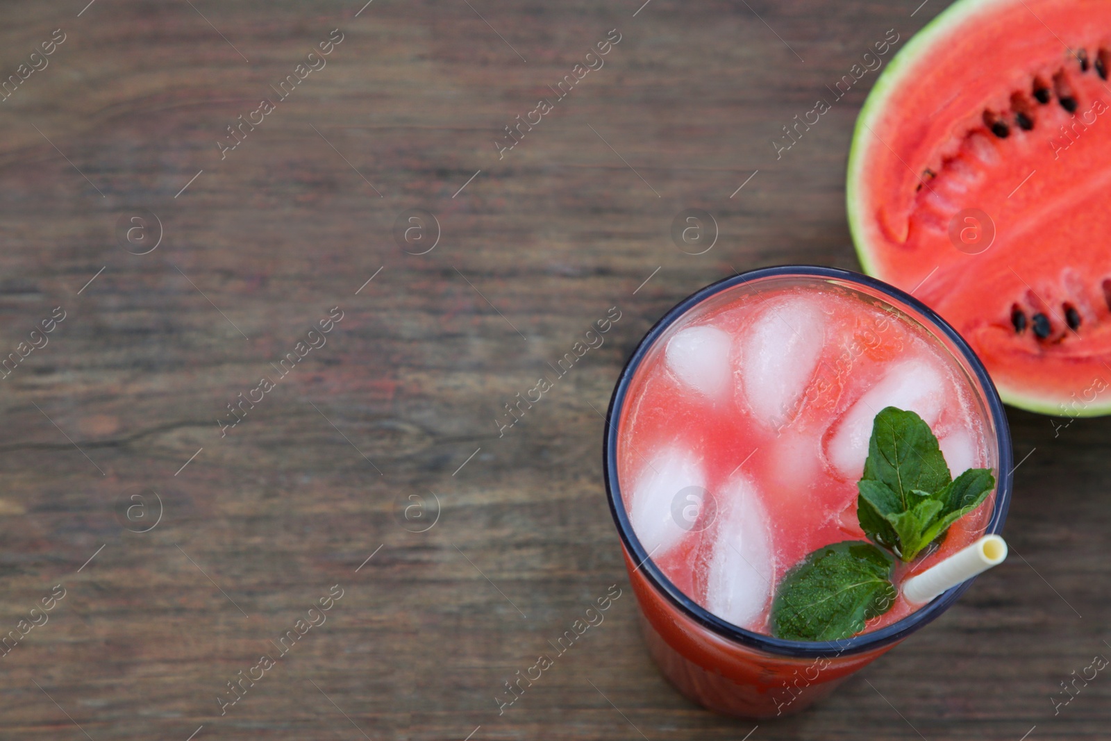 Photo of Glass of delicious watermelon drink with mint, ice cubes and fresh cut fruit on wooden table, top view. Space for text