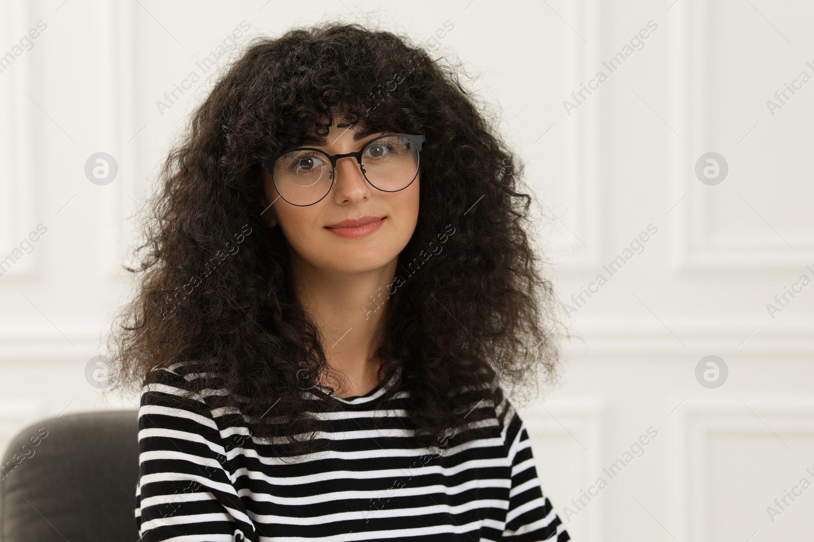 Photo of Portrait of beautiful woman with curly hair sitting on armchair indoors. Attractive lady looking at camera