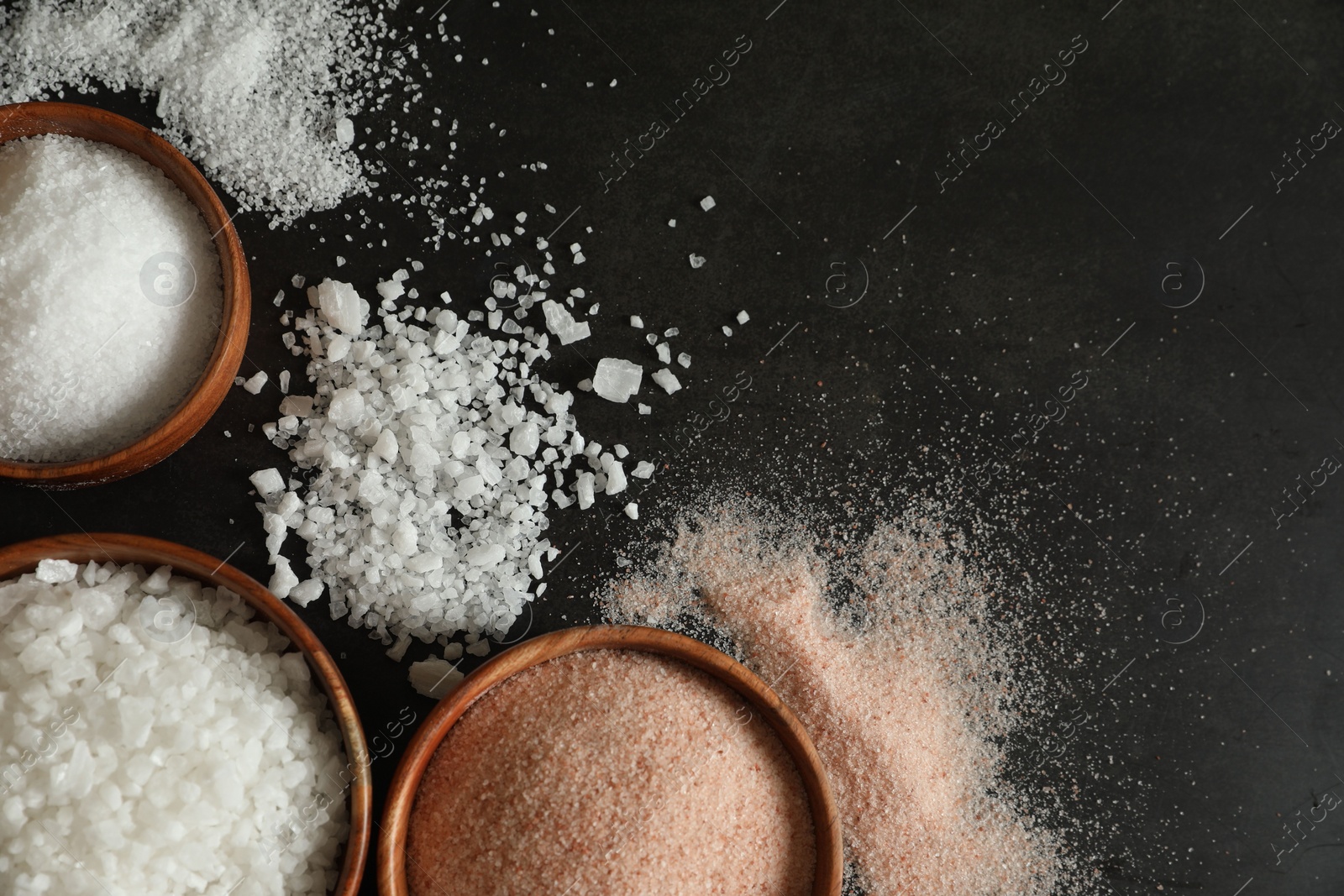 Photo of Different types of organic salt in bowls on black table, flat lay. Space for text