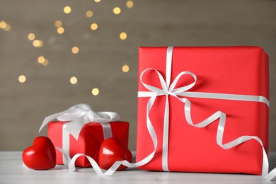 Photo of Beautiful gift boxes with decorative red hearts on white wooden table against blurred lights