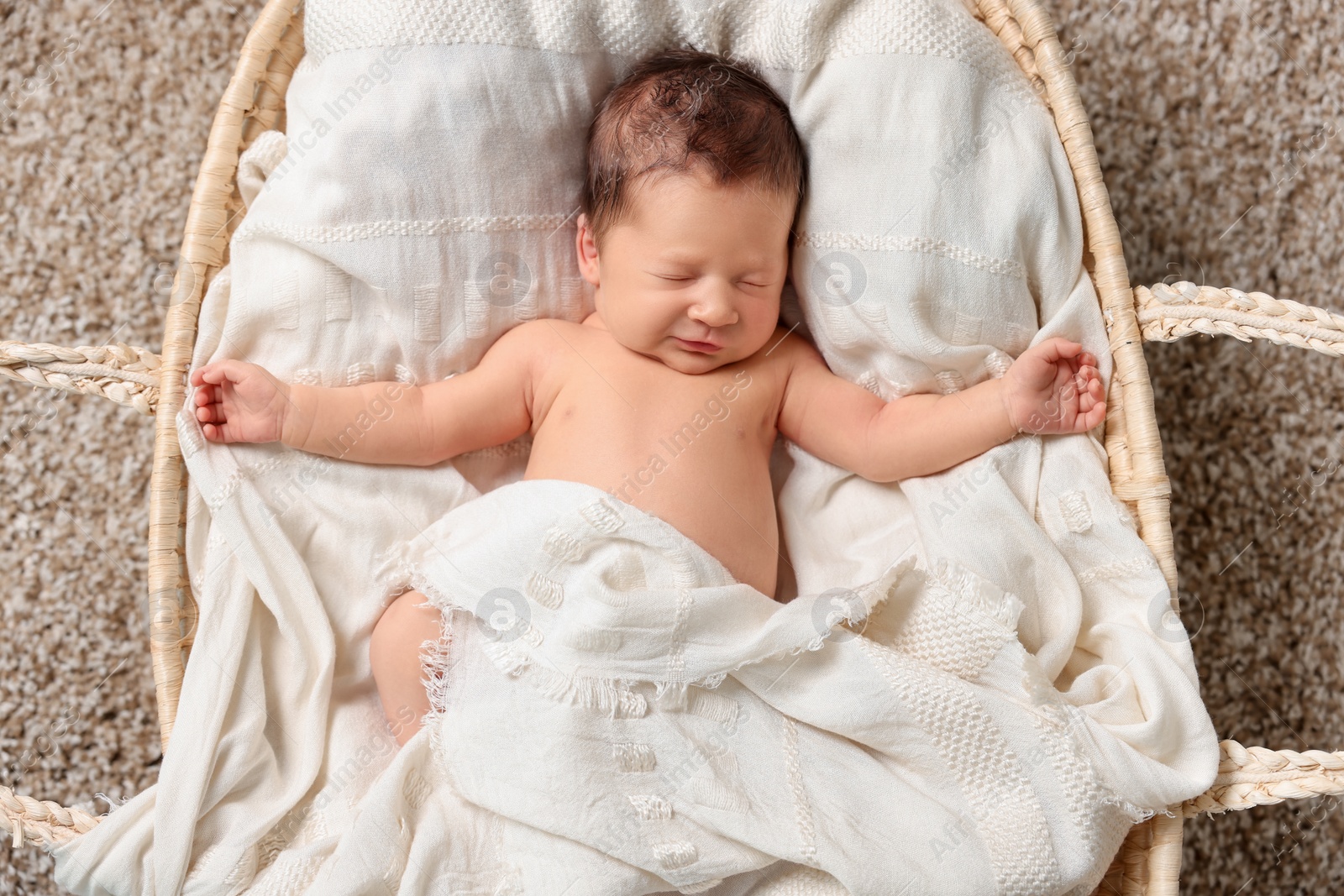 Photo of Cute newborn baby sleeping on white blanket in wicker crib, top view