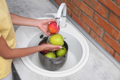 Woman washing fresh apples in kitchen sink, closeup