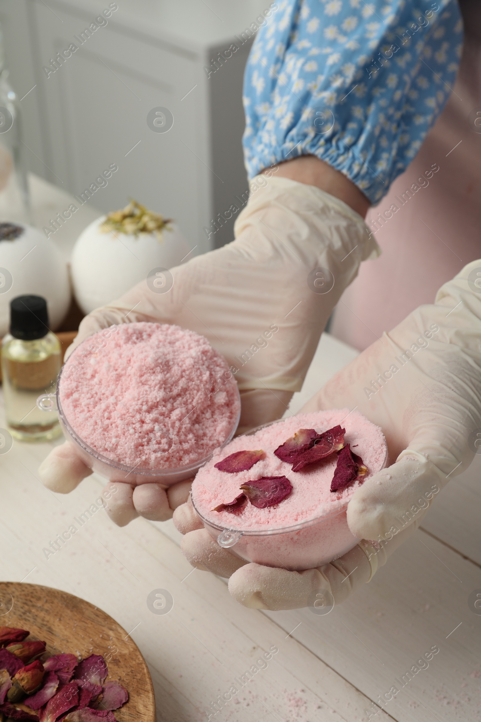 Photo of Woman in gloves making bath bomb at white table indoors, closeup