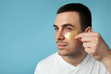 Photo of Young man applying under eye patches on light blue background. Space for text