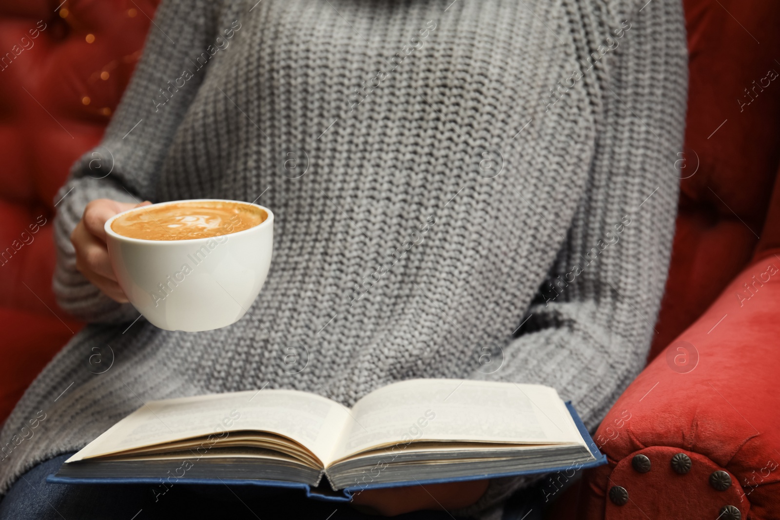 Photo of Woman with cup of coffee reading book on sofa, closeup