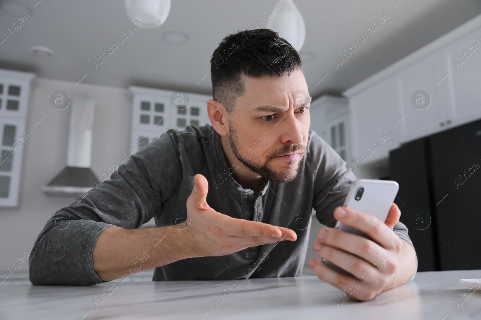 Photo of Emotional man with smartphone at table in kitchen. Online hate concept