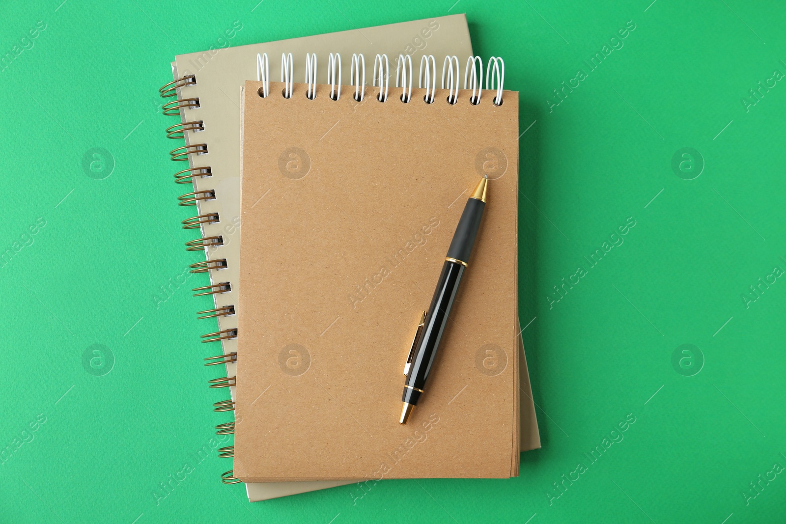 Photo of Notebooks and pen on green background, top view