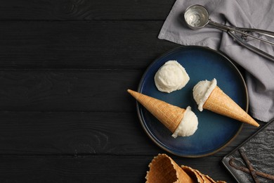 Photo of Ice cream scoops in wafer cones on black wooden table, flat lay. Space for text