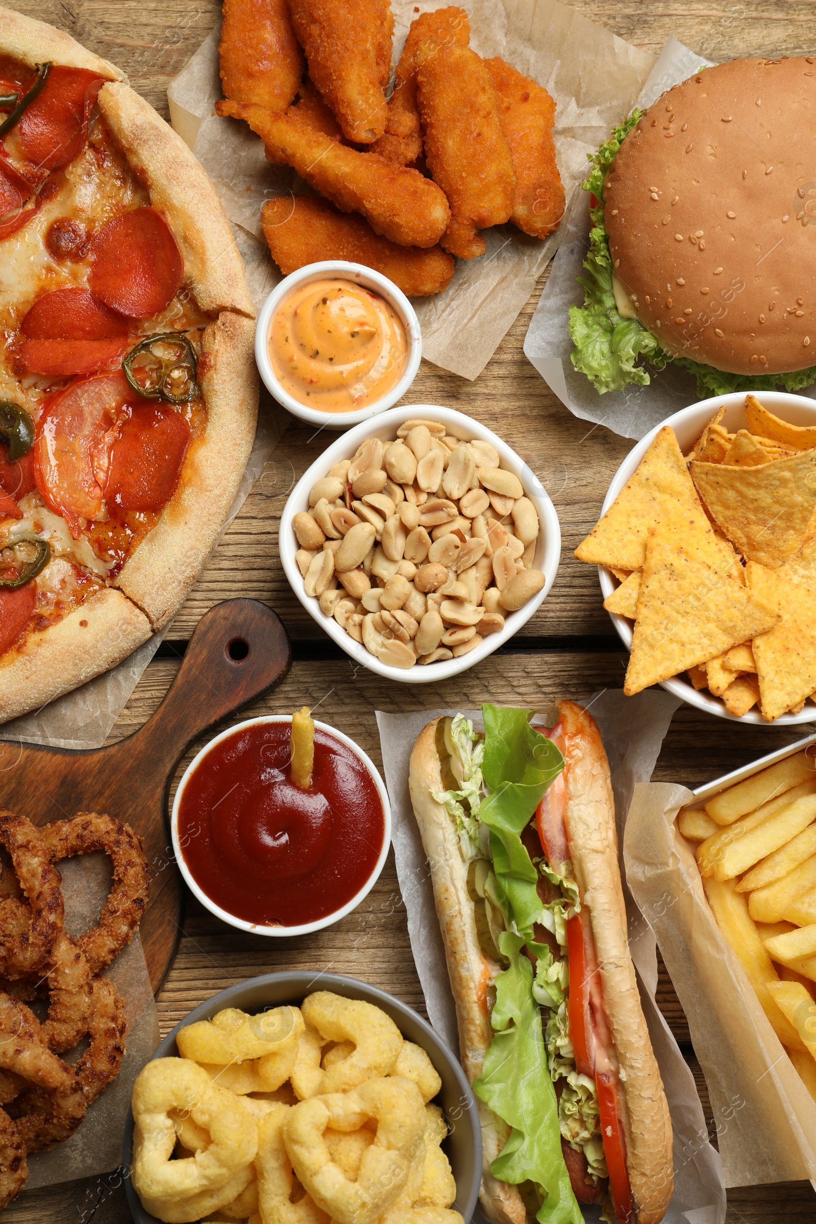 Photo of Onion rings, sandwich and other fast food on wooden table, flat lay