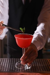 Photo of Bartender preparing fresh Martini cocktail in glass at bar counter, closeup