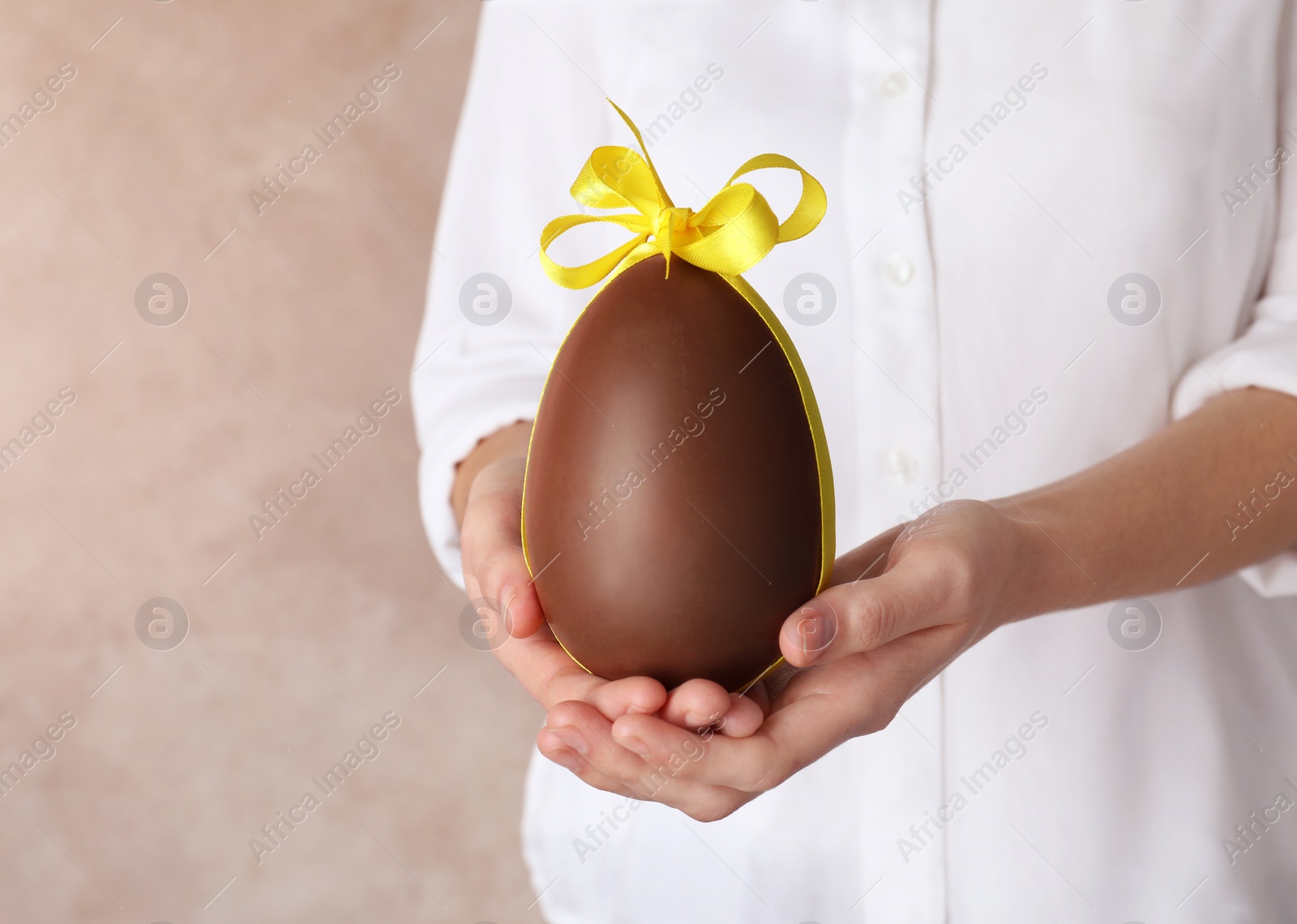 Photo of Woman holding chocolate Easter egg with bow knot on color background, closeup